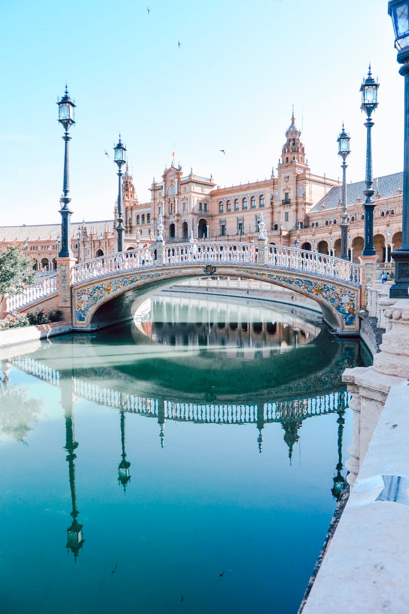 Explore the stunning architecture of Plaza de España in Seville, featuring a beautiful bridge and canal reflection.