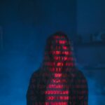 A mysterious silhouette with red binary code projected over the face, set against a dark, moody background.